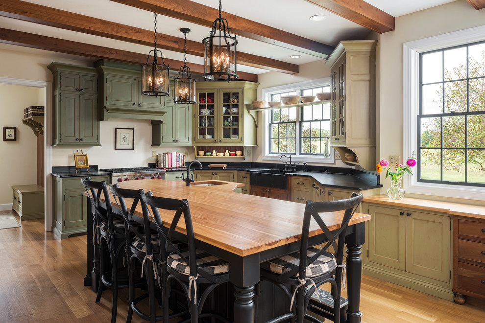 Kitchen - traditional l-shaped medium tone wood floor kitchen idea in St Louis with a farmhouse sink, shaker cabinets, green cabinets, stainless steel appliances, an island and soapstone countertops