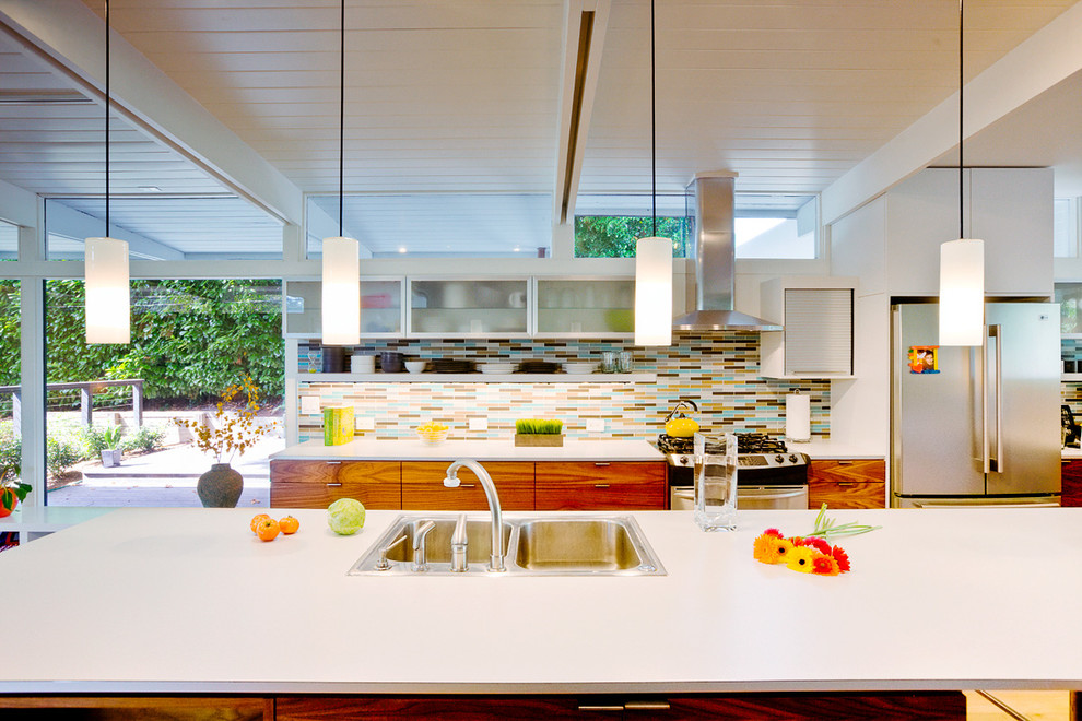 Bild på ett funkis kök, med en nedsänkt diskho, släta luckor, skåp i mellenmörkt trä, laminatbänkskiva, flerfärgad stänkskydd, stänkskydd i glaskakel och rostfria vitvaror