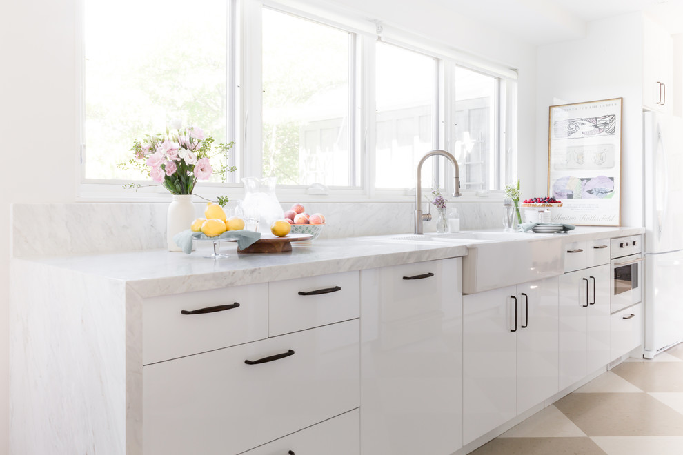 Inspiration för mellanstora moderna kök, med en rustik diskho, släta luckor, vita skåp, marmorbänkskiva, grått stänkskydd, stänkskydd i marmor, vita vitvaror, linoleumgolv, en köksö och beiget golv