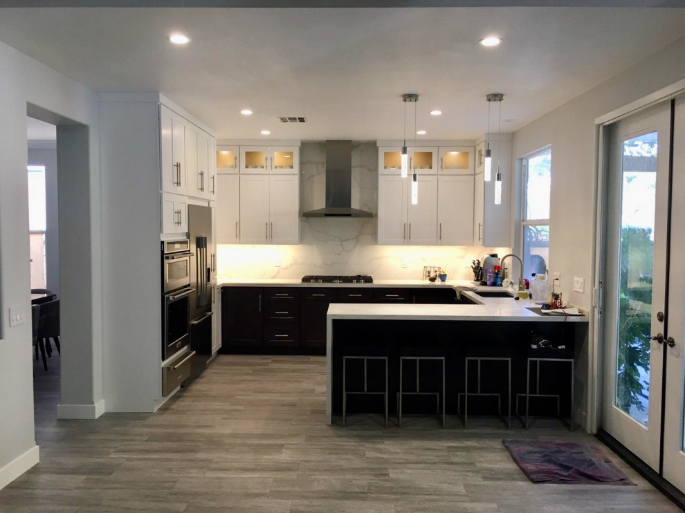 This is an example of an u-shaped kitchen/diner in Los Angeles with a submerged sink, shaker cabinets, brown cabinets, quartz worktops, multi-coloured splashback, porcelain splashback, stainless steel appliances, laminate floors, an island, grey floors and multicoloured worktops.