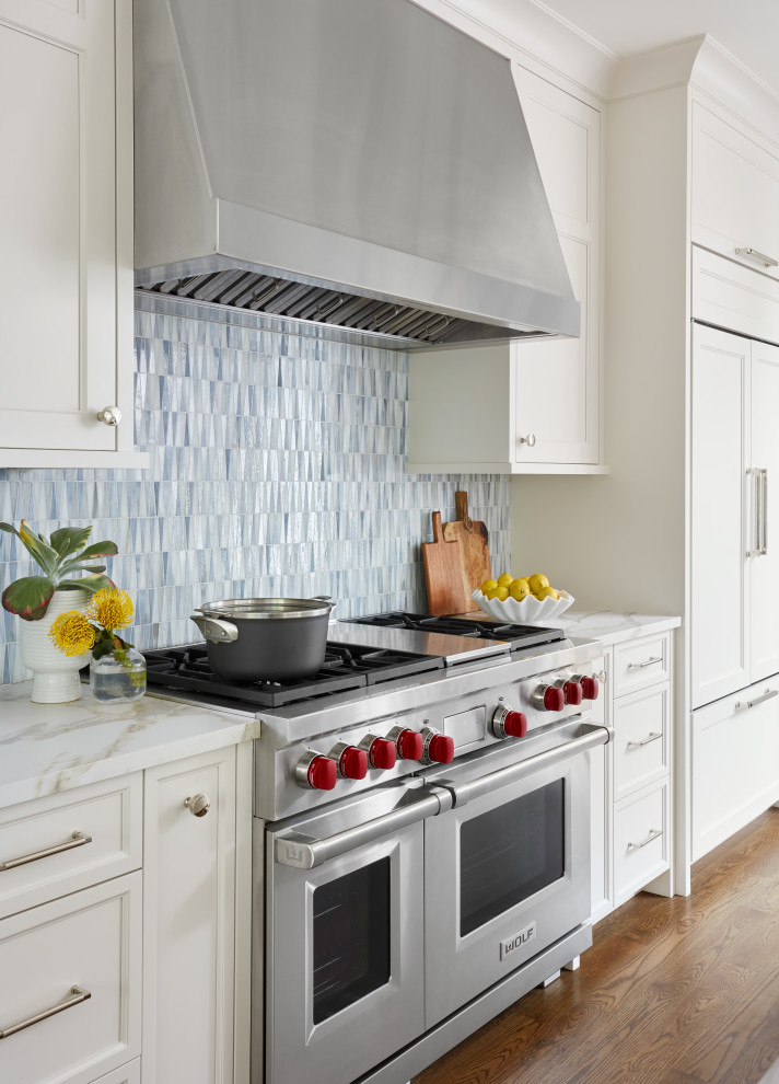 Modern inredning av ett kök, med vita skåp, blått stänkskydd, rostfria vitvaror och en köksö