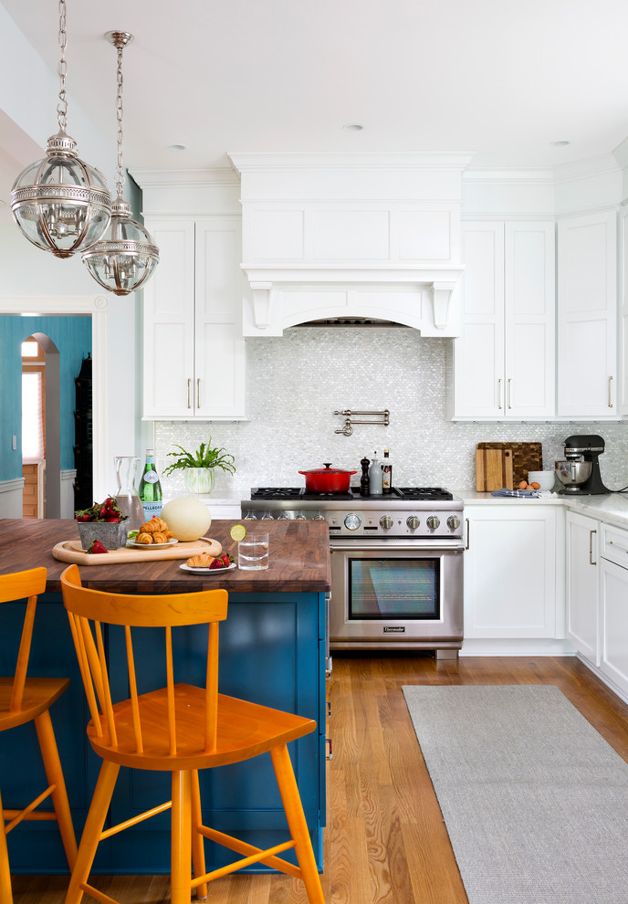 Modelo de cocina comedor clásica renovada grande con puertas de armario azules, salpicadero blanco, electrodomésticos de acero inoxidable, suelo de madera en tonos medios y una isla