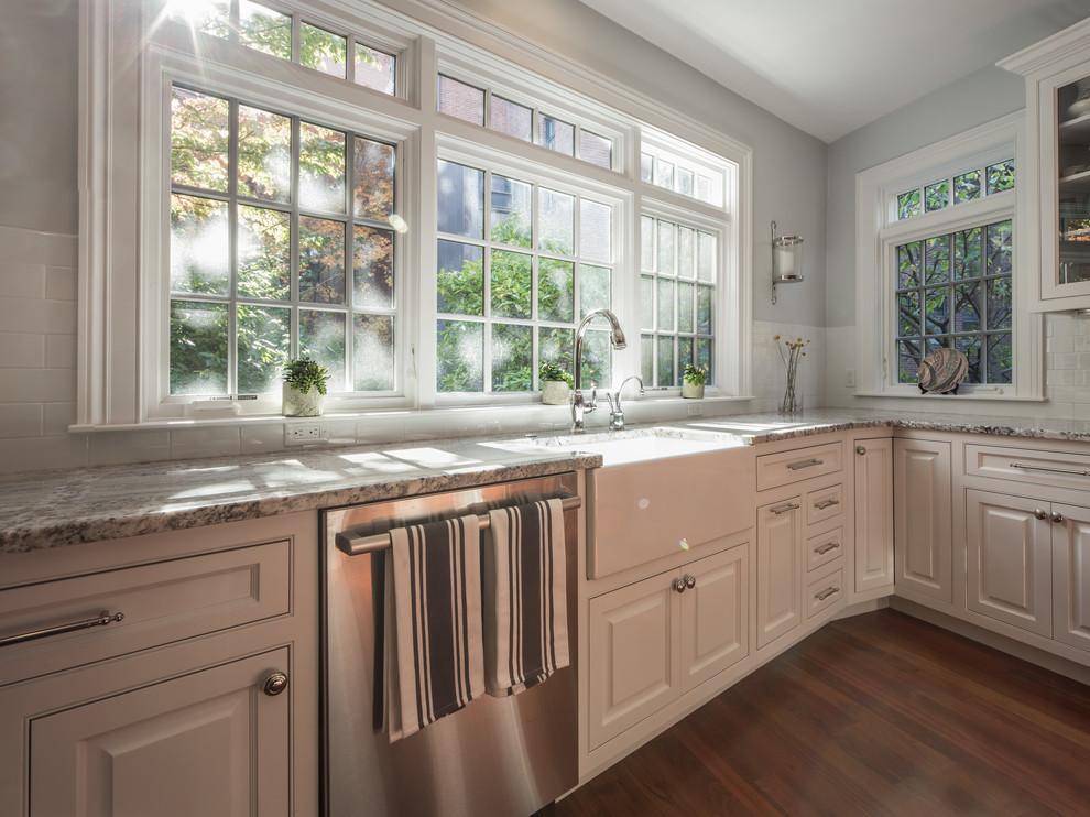 Mid-sized transitional l-shaped medium tone wood floor and brown floor eat-in kitchen photo in Boston with a farmhouse sink, raised-panel cabinets, white cabinets, granite countertops, white backsplash, subway tile backsplash, stainless steel appliances and a peninsula