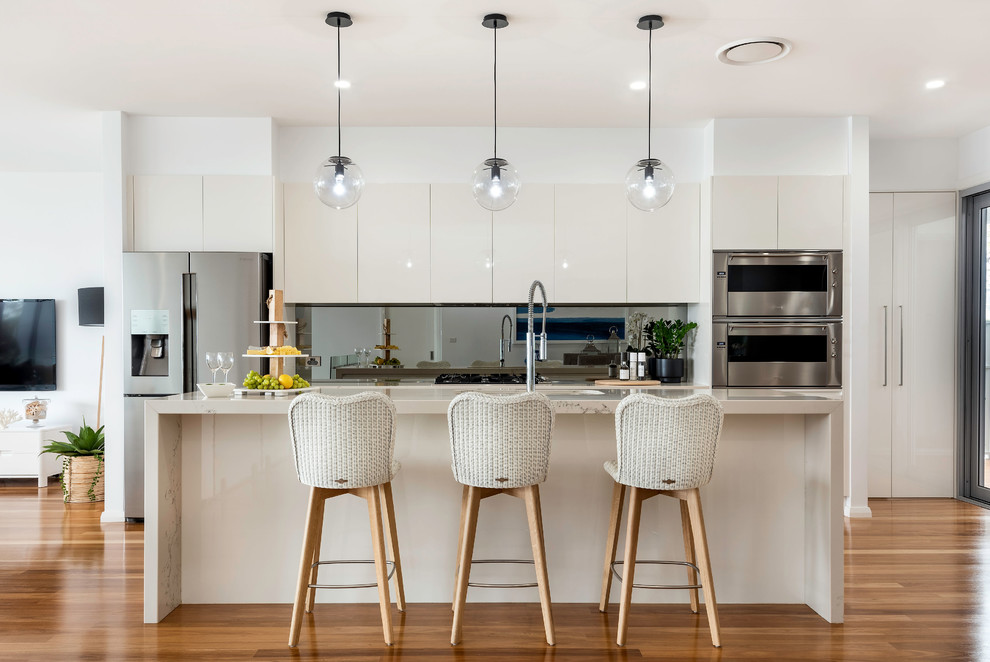 Foto di una cucina parallela minimal con ante a filo, ante beige, elettrodomestici in acciaio inossidabile, pavimento in legno massello medio, pavimento marrone e top beige