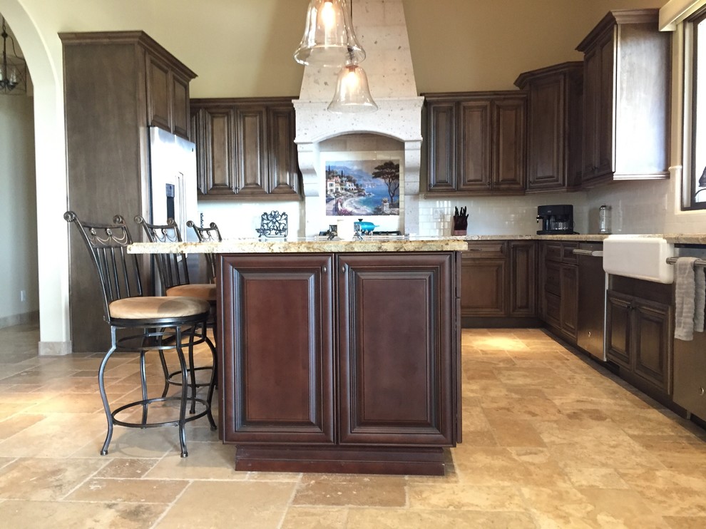 Inredning av ett klassiskt stort beige beige kök, med en rustik diskho, luckor med upphöjd panel, skåp i mörkt trä, granitbänkskiva, beige stänkskydd, stänkskydd i travertin, rostfria vitvaror, travertin golv, en köksö och beiget golv