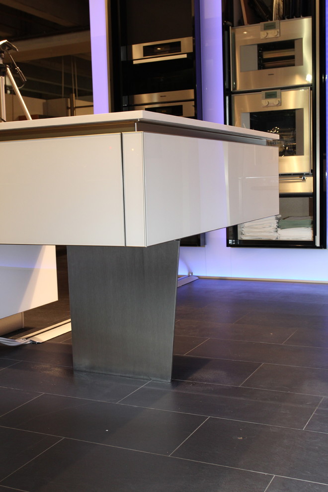 This is an example of an expansive urban l-shaped open plan kitchen in Munich with a submerged sink, glass-front cabinets, white cabinets, engineered stone countertops, stainless steel appliances, glass sheet splashback, limestone flooring and multiple islands.