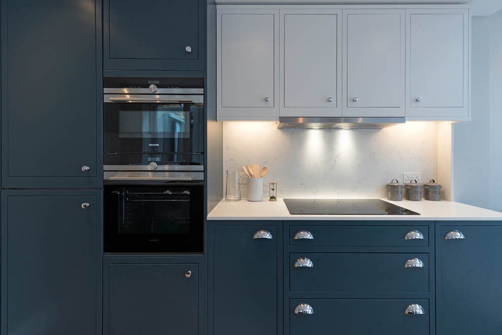 Example of a mid-sized ornate galley light wood floor and beige floor open concept kitchen design in London with a drop-in sink, shaker cabinets, blue cabinets, solid surface countertops, white backsplash, marble backsplash, black appliances and no island