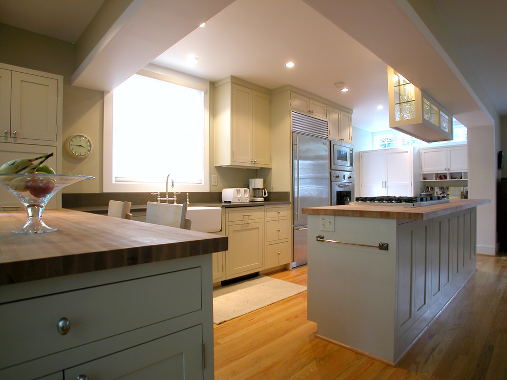 Foto på ett funkis kök, med en rustik diskho, luckor med infälld panel, vita skåp, träbänkskiva, grått stänkskydd, rostfria vitvaror, mellanmörkt trägolv och en köksö
