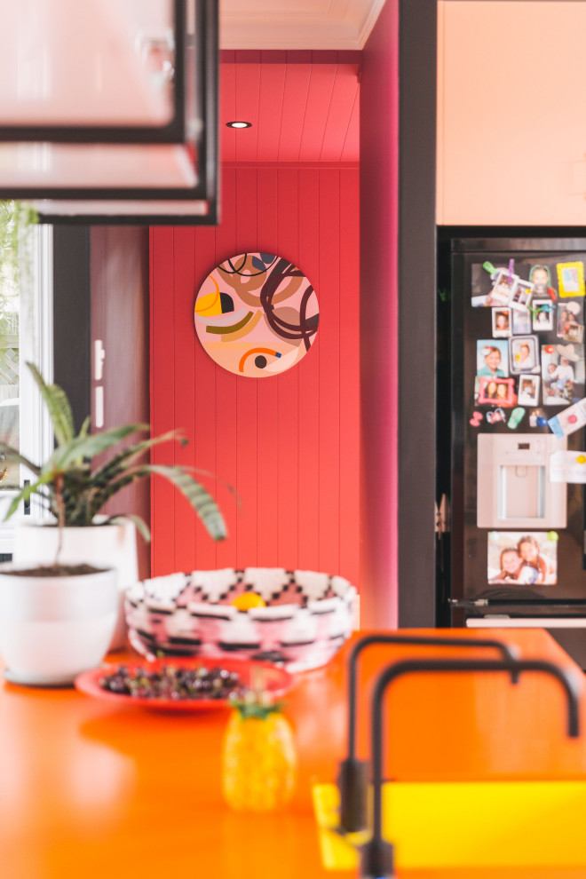 Moderne Küche mit Unterbauwaschbecken, Laminat-Arbeitsplatte, Küchenrückwand in Weiß, Rückwand aus Keramikfliesen, schwarzen Elektrogeräten, gebeiztem Holzboden, Kücheninsel, rosa Boden und oranger Arbeitsplatte in Sonstige