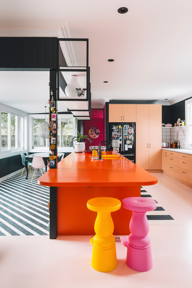Idéer för funkis oranget kök, med en undermonterad diskho, laminatbänkskiva, vitt stänkskydd, stänkskydd i keramik, svarta vitvaror, målat trägolv, en köksö och rosa golv
