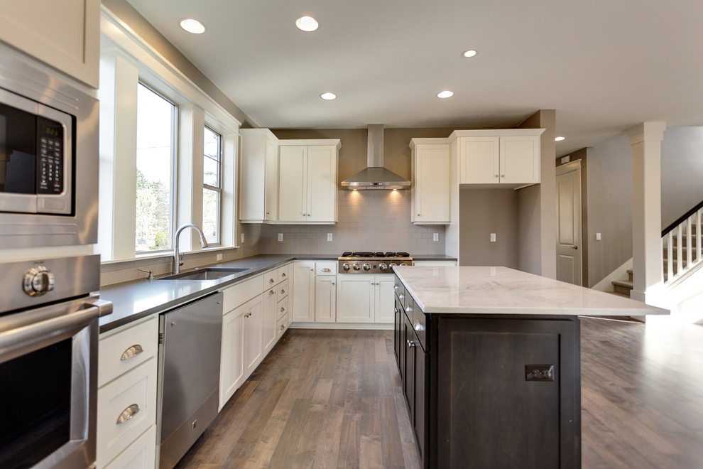 Exempel på ett mellanstort amerikanskt kök, med en enkel diskho, luckor med infälld panel, skåp i mörkt trä, bänkskiva i kvarts, grått stänkskydd, stänkskydd i keramik, rostfria vitvaror, mellanmörkt trägolv och en köksö