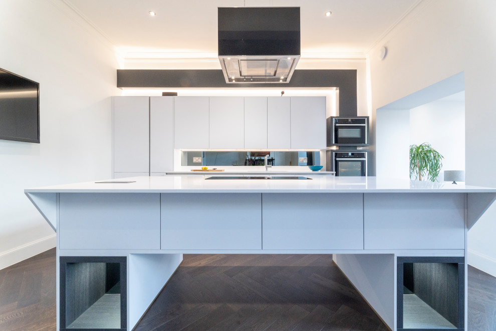 Example of a large trendy single-wall medium tone wood floor and brown floor eat-in kitchen design in Edinburgh with a drop-in sink, flat-panel cabinets, white cabinets, quartzite countertops, black backsplash, mirror backsplash, black appliances, an island and white countertops