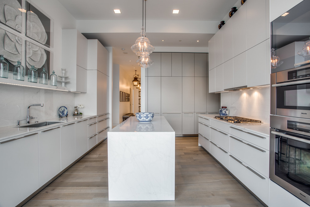 Mid-sized trendy galley medium tone wood floor and brown floor eat-in kitchen photo in Dallas with an undermount sink, flat-panel cabinets, white cabinets, solid surface countertops, white backsplash, an island and white countertops