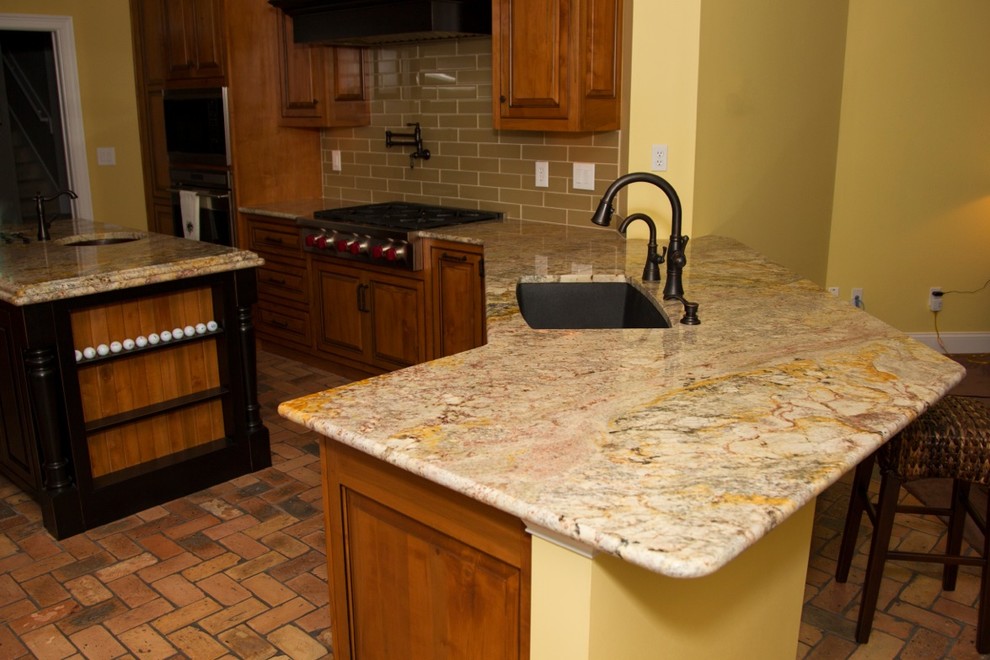 Cette image montre une cuisine ouverte parallèle traditionnelle de taille moyenne avec un évier intégré, un plan de travail en granite, une crédence beige, un électroménager en acier inoxydable, tomettes au sol et îlot.