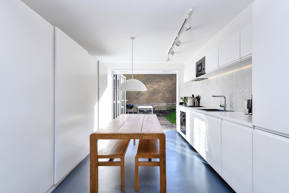 Modelo de cocina comedor contemporánea de tamaño medio sin isla con fregadero de un seno, armarios con paneles lisos, puertas de armario blancas, encimera de laminado, salpicadero blanco, salpicadero de azulejos de cerámica, electrodomésticos de acero inoxidable, suelo de linóleo, suelo gris y encimeras blancas