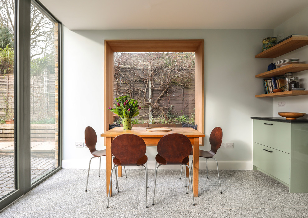 This is an example of a medium sized contemporary single-wall open plan kitchen in London with a built-in sink, flat-panel cabinets, green cabinets, composite countertops, black splashback, ceramic splashback, stainless steel appliances, terrazzo flooring, grey floors and black worktops.