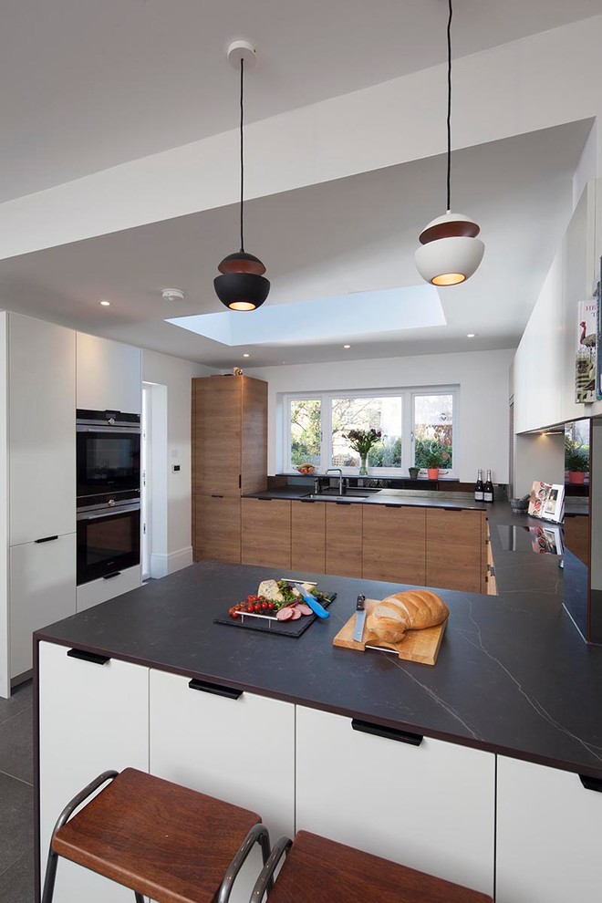 Inspiration for a medium sized victorian u-shaped open plan kitchen in London with a built-in sink, flat-panel cabinets, medium wood cabinets, integrated appliances, ceramic flooring, a breakfast bar, grey floors and black worktops.