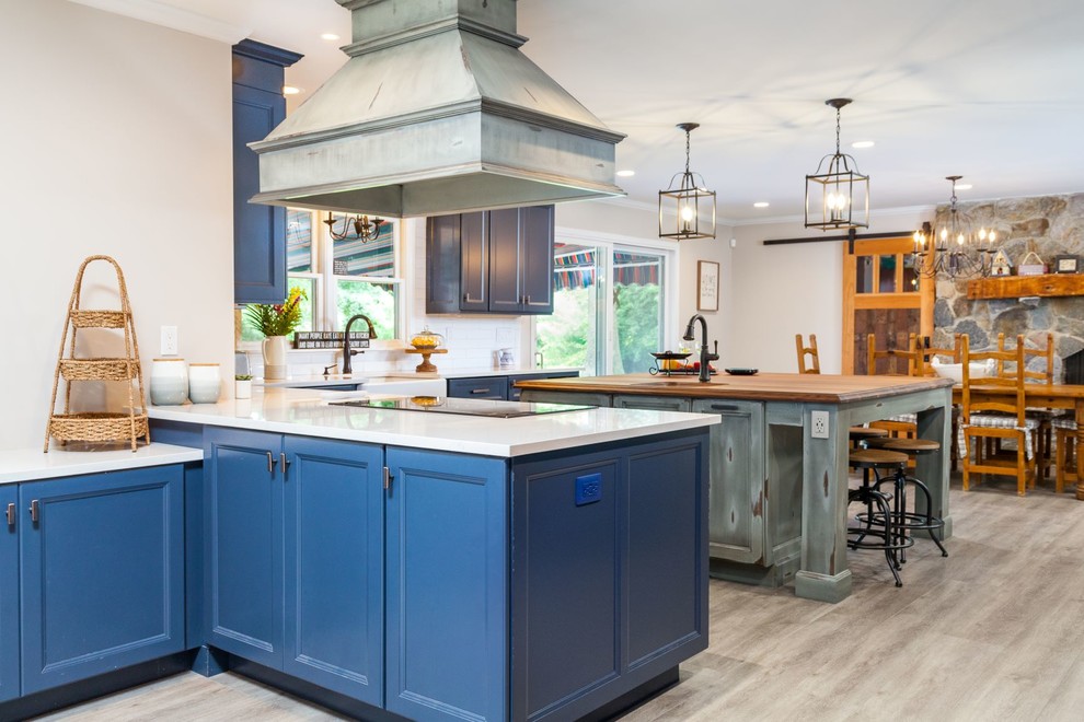 Foto på ett stort lantligt vit kök, med en rustik diskho, luckor med profilerade fronter, blå skåp, bänkskiva i kvartsit, vitt stänkskydd, stänkskydd i porslinskakel, svarta vitvaror, vinylgolv, en köksö och grått golv