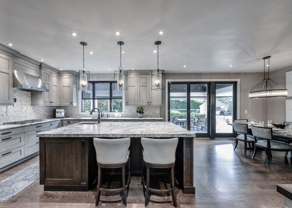 Large trendy l-shaped dark wood floor and brown floor eat-in kitchen photo with an integrated sink, recessed-panel cabinets, gray cabinets, quartzite countertops, gray backsplash, mosaic tile backsplash, stainless steel appliances and an island