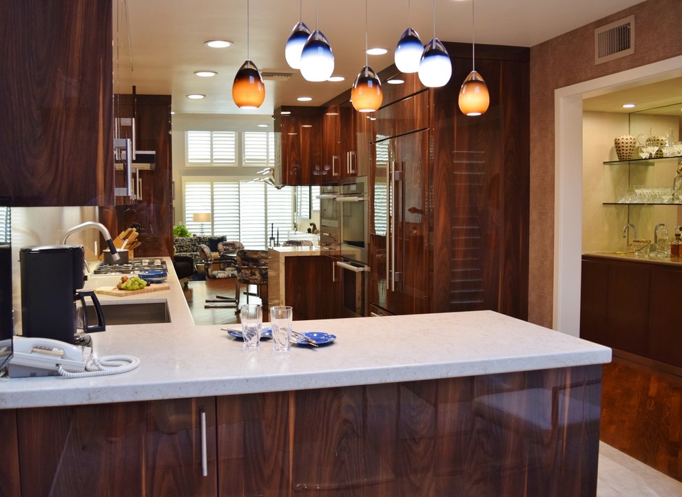 This is an example of a medium sized contemporary galley kitchen in Los Angeles with a belfast sink, flat-panel cabinets, dark wood cabinets, engineered stone countertops, beige splashback, stone slab splashback, coloured appliances, light hardwood flooring and beige floors.
