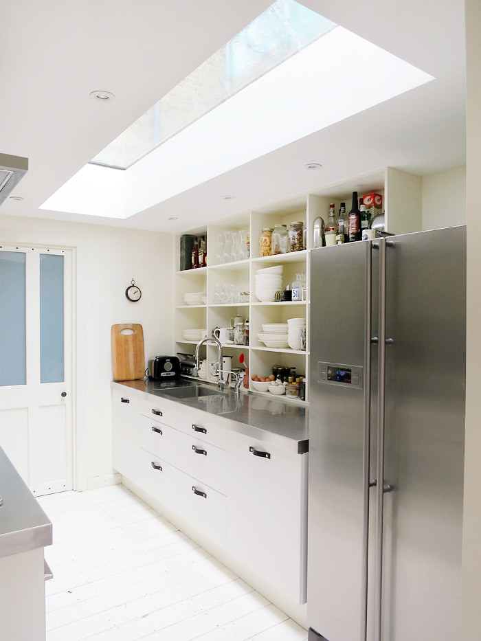 Modelo de cocina ecléctica con fregadero integrado, armarios abiertos, puertas de armario blancas y encimera de acero inoxidable