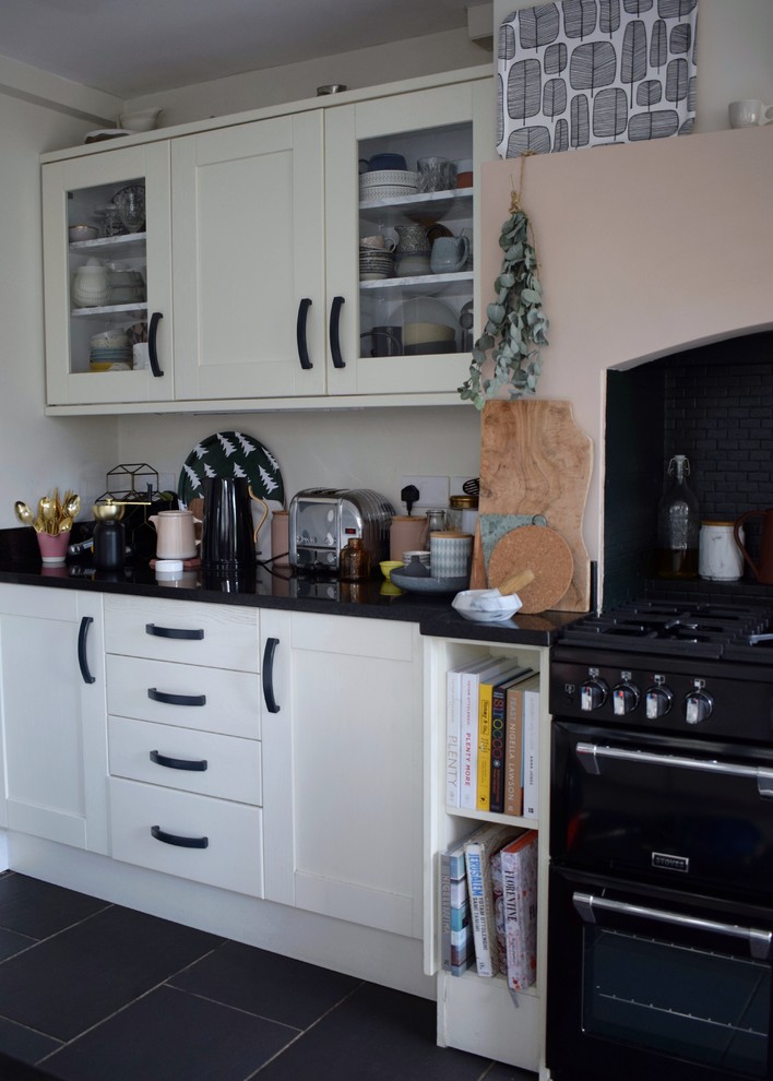 This is an example of a medium sized kitchen/diner in London with a built-in sink, recessed-panel cabinets, white cabinets, granite worktops, black appliances, limestone flooring, no island and black floors.