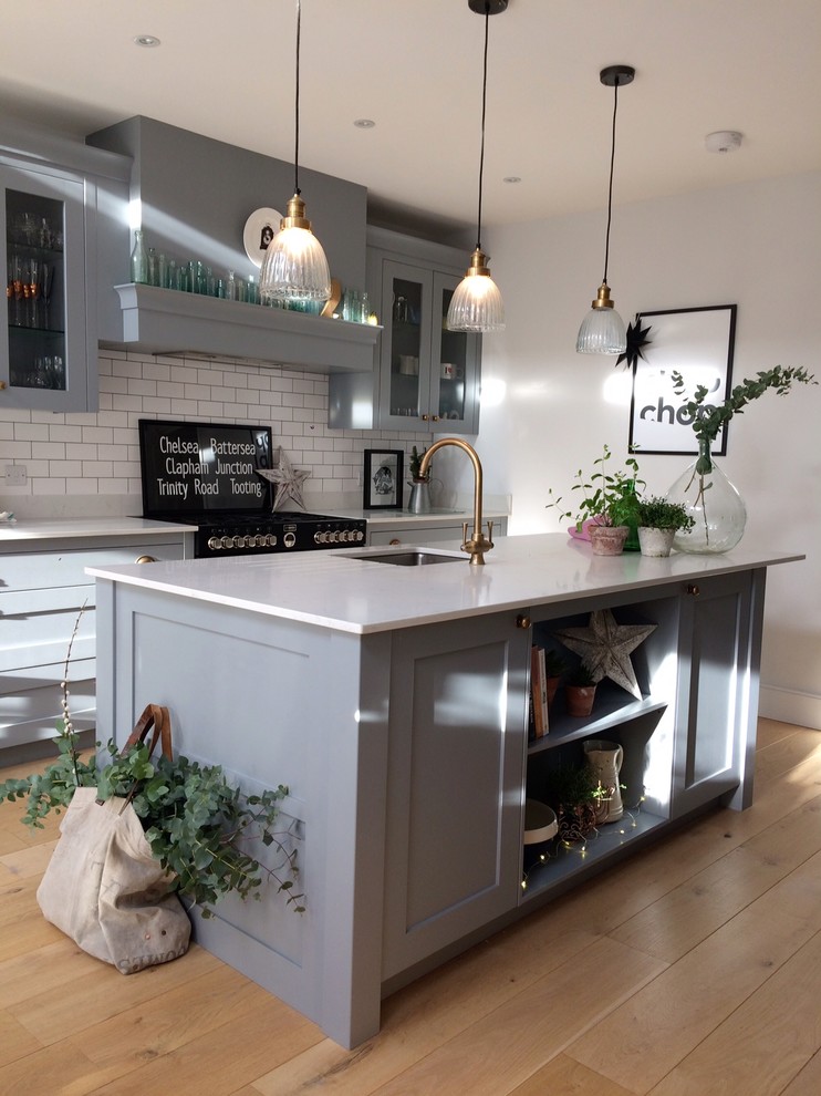 Design ideas for a medium sized contemporary u-shaped kitchen/diner in Surrey with a submerged sink, shaker cabinets, grey cabinets, granite worktops, white splashback, ceramic splashback, black appliances, light hardwood flooring, an island and brown floors.