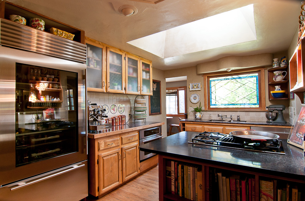 Exemple d'une cuisine chic en bois clair avec un placard à porte vitrée, une crédence beige et un électroménager en acier inoxydable.