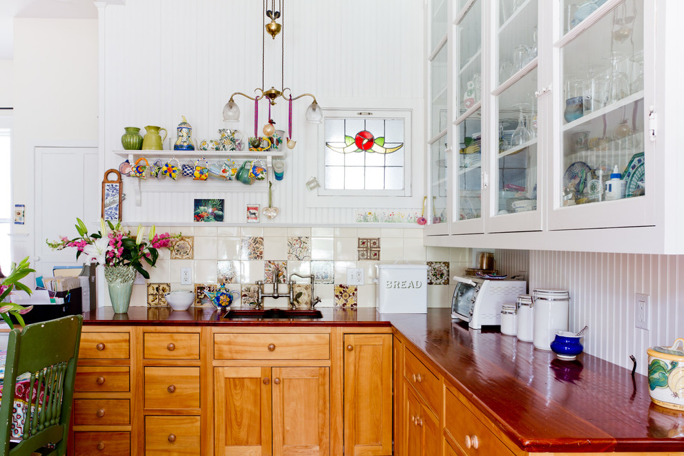 На фото: кухня в викторианском стиле с стеклянными фасадами, белыми фасадами, деревянной столешницей, разноцветным фартуком и красивой плиткой