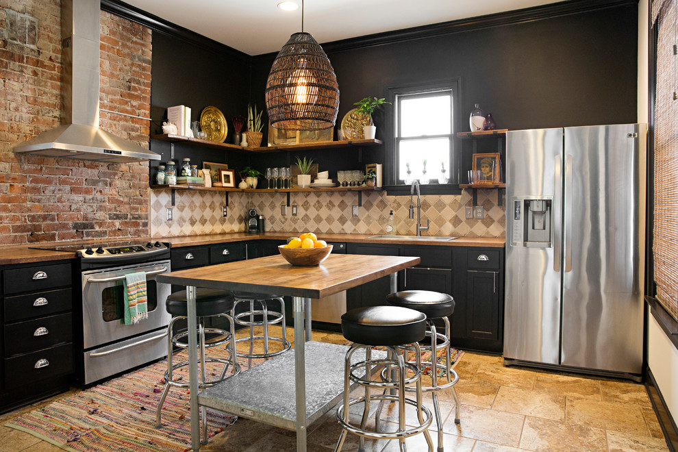 This is an example of a bohemian l-shaped kitchen in Nashville with a built-in sink, recessed-panel cabinets, black cabinets, wood worktops, beige splashback, stainless steel appliances, an island, brown floors and brown worktops.