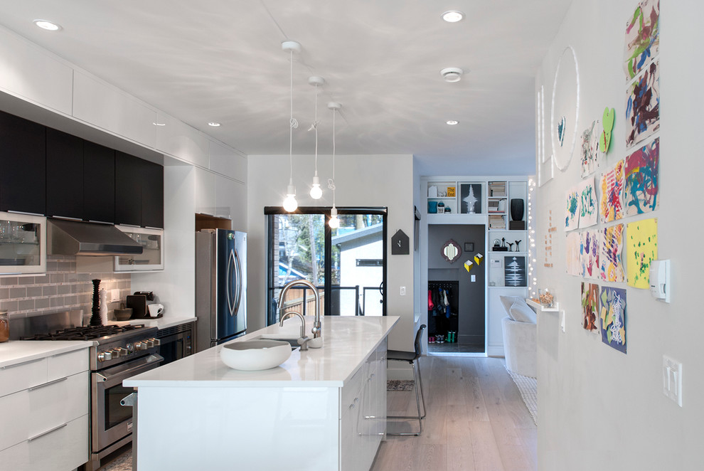 Kitchen - contemporary galley medium tone wood floor kitchen idea in Vancouver with flat-panel cabinets, white cabinets, gray backsplash, stainless steel appliances and an island