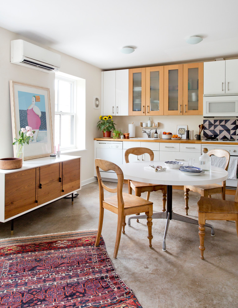 Modelo de cocina lineal contemporánea con fregadero encastrado, armarios con paneles lisos, puertas de armario blancas, encimera de madera, electrodomésticos blancos y suelo de cemento