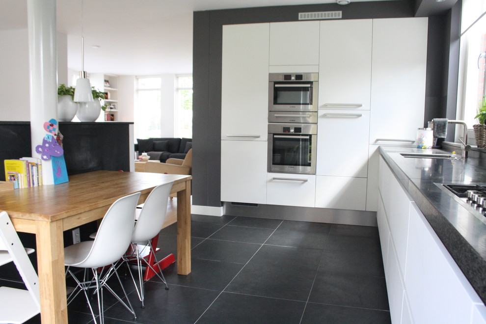 На фото: угловая кухня в современном стиле с техникой из нержавеющей стали, плоскими фасадами, белыми фасадами и серым полом