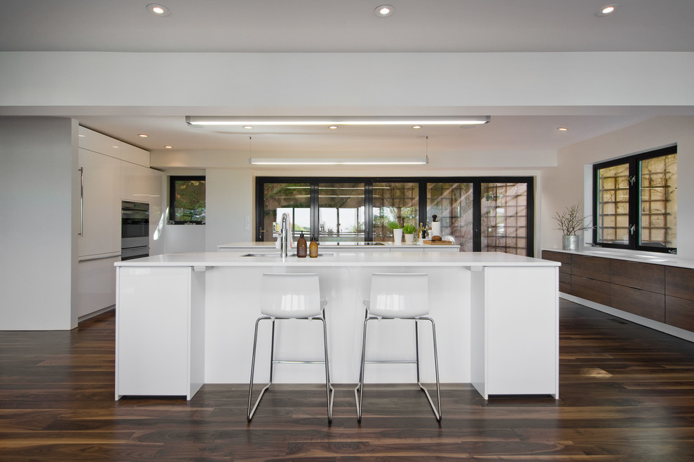 Пример оригинального дизайна: кухня-гостиная в стиле модернизм с белыми фасадами, плоскими фасадами и техникой под мебельный фасад