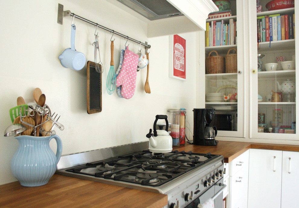 Eklektisk inredning av ett kök, med luckor med glaspanel, vita skåp, träbänkskiva och rostfria vitvaror