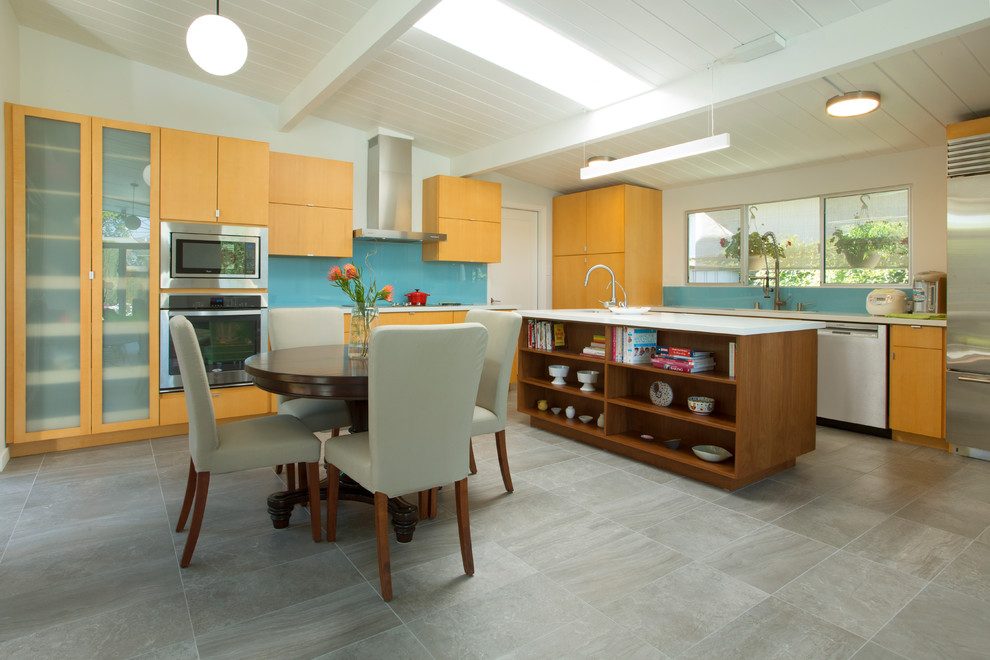 This is an example of a midcentury kitchen/diner in San Francisco with flat-panel cabinets, medium wood cabinets, blue splashback, stainless steel appliances, an island, grey floors and glass sheet splashback.