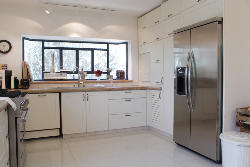 Bohemian u-shaped kitchen in Tel Aviv with white cabinets, beige splashback and stainless steel appliances.