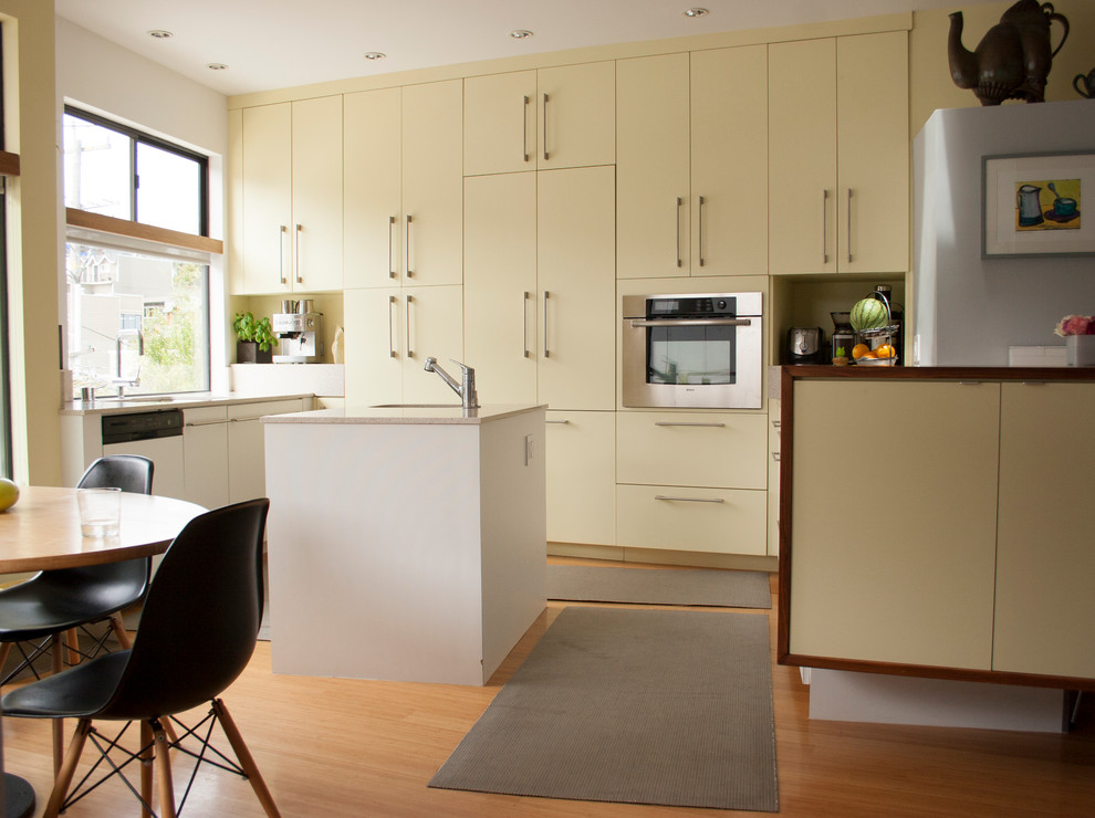Diseño de cocina contemporánea con armarios con paneles lisos, puertas de armario beige, suelo de madera clara y una isla