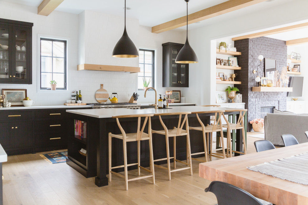 This is an example of a scandinavian open plan kitchen in Chicago with black cabinets, white splashback, metro tiled splashback, light hardwood flooring, an island, white worktops, exposed beams and shaker cabinets.