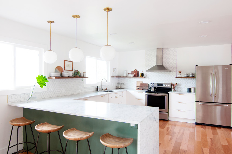 Bild på ett mellanstort 50 tals kök, med en enkel diskho, släta luckor, vita skåp, marmorbänkskiva, vitt stänkskydd, stänkskydd i porslinskakel, rostfria vitvaror, ljust trägolv och en halv köksö