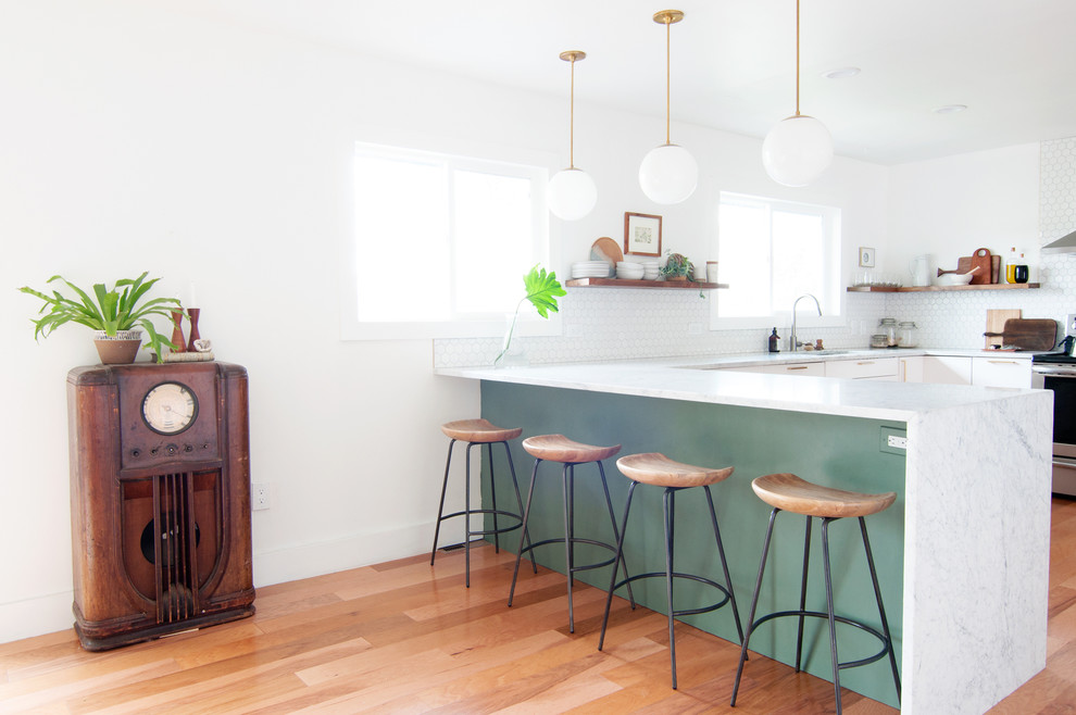 Bild på ett mellanstort retro kök, med en enkel diskho, släta luckor, vita skåp, marmorbänkskiva, vitt stänkskydd, stänkskydd i porslinskakel, rostfria vitvaror, ljust trägolv och en halv köksö