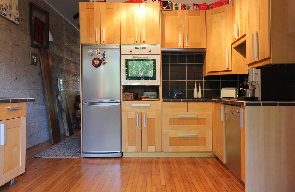 Foto på ett eklektiskt kök, med luckor med infälld panel, skåp i ljust trä, kaklad bänkskiva, svart stänkskydd, stänkskydd i keramik och rostfria vitvaror