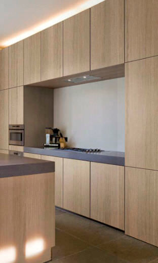 Modern inredning av ett kök, med släta luckor, skåp i ljust trä, rostfria vitvaror, betonggolv, en köksö och brunt golv