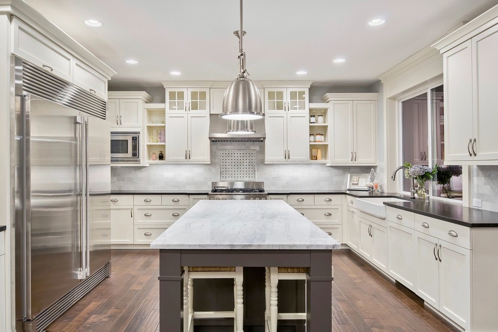 Design ideas for a classic grey and cream u-shaped kitchen in Los Angeles with a belfast sink, beaded cabinets, white cabinets, grey splashback, metro tiled splashback, stainless steel appliances, medium hardwood flooring, an island, brown floors and black worktops.