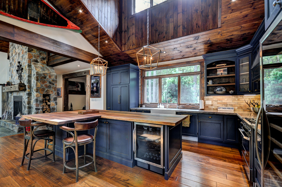 This is an example of a rustic l-shaped open plan kitchen in Toronto with a belfast sink, shaker cabinets, blue cabinets, beige splashback, stainless steel appliances, medium hardwood flooring, an island, brown floors and grey worktops.