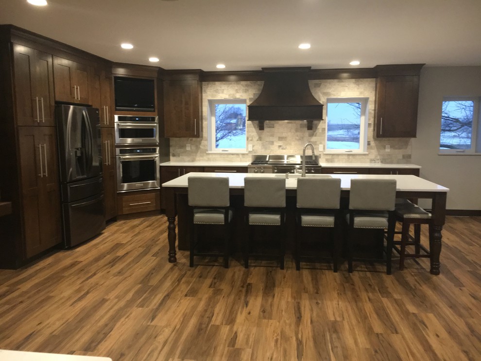 Example of a large classic vinyl floor and brown floor kitchen design in Cedar Rapids with a single-bowl sink, shaker cabinets, dark wood cabinets, quartz countertops, gray backsplash, marble backsplash, stainless steel appliances, an island and white countertops