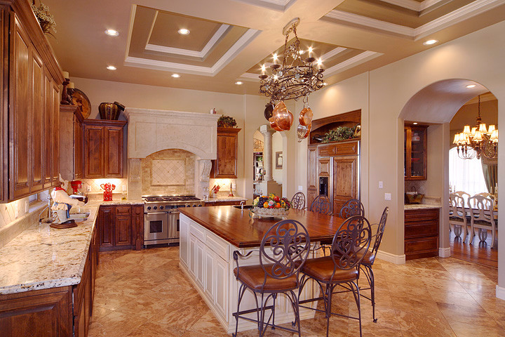 Mid-sized tuscan l-shaped travertine floor and brown floor enclosed kitchen photo in Phoenix with a double-bowl sink, raised-panel cabinets, medium tone wood cabinets, laminate countertops, beige backsplash, stone tile backsplash, stainless steel appliances and an island