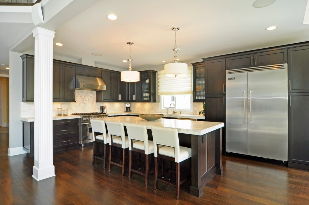 Example of a mid-sized transitional l-shaped dark wood floor open concept kitchen design in Chicago with an undermount sink, shaker cabinets, dark wood cabinets, solid surface countertops, beige backsplash, stone slab backsplash, stainless steel appliances and an island