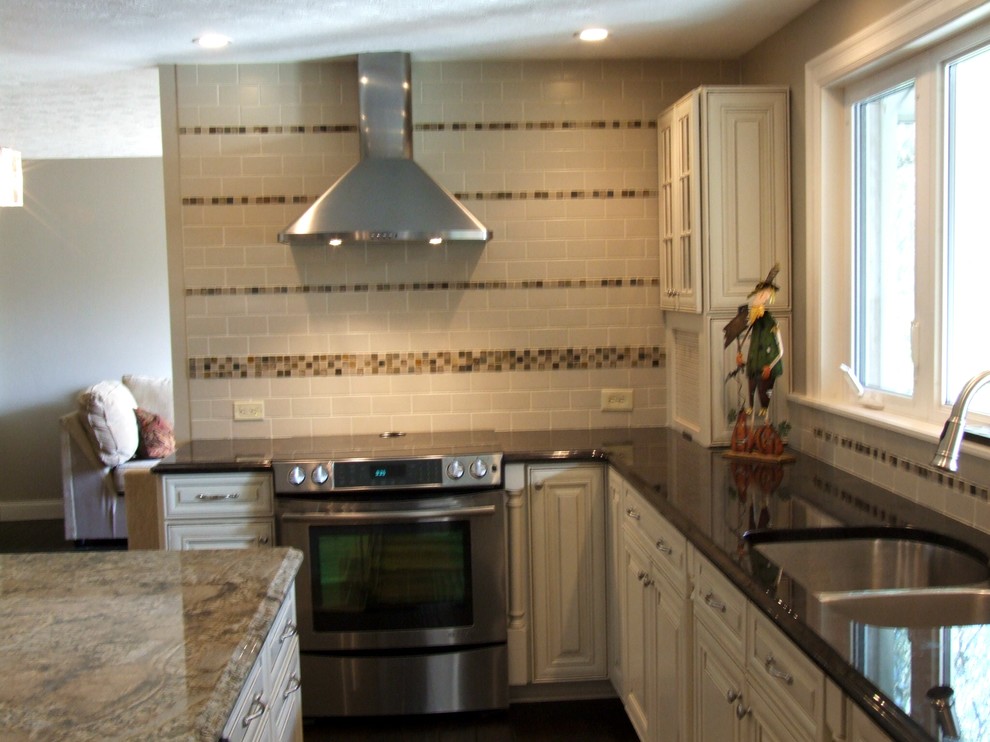 Mittelgroße Klassische Küche in L-Form mit weißen Schränken, Granit-Arbeitsplatte, Küchenrückwand in Beige, Küchengeräten aus Edelstahl, dunklem Holzboden und Kücheninsel in Cleveland