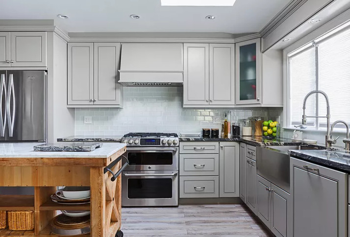 Bild på ett avskilt, mellanstort lantligt svart svart l-kök, med en rustik diskho, luckor med upphöjd panel, grå skåp, granitbänkskiva, grått stänkskydd, stänkskydd i glaskakel, rostfria vitvaror, vinylgolv, en köksö och flerfärgat golv